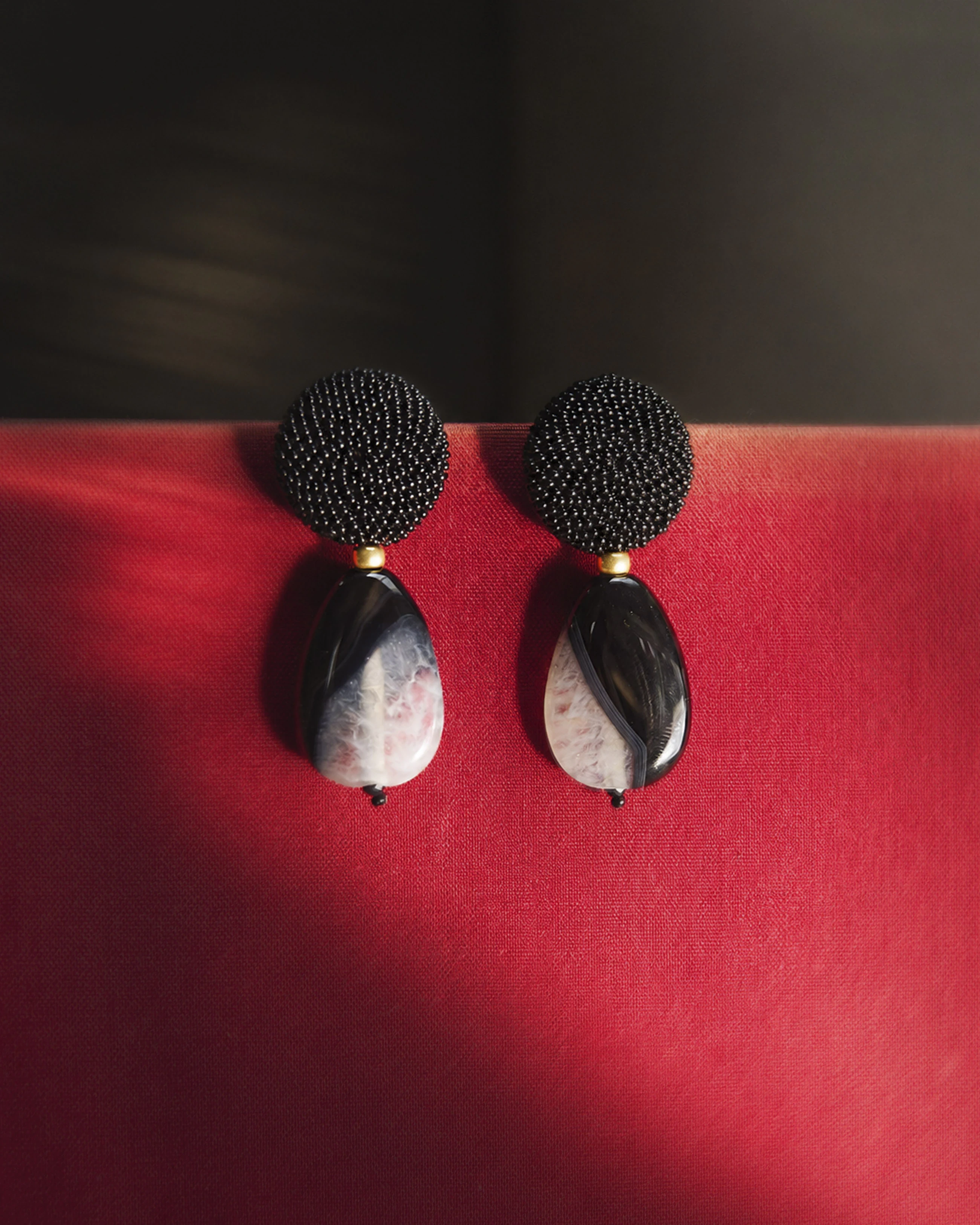 Black & White Agate Drop Earrings with Black Beaded Round Top — pair of drop earrings with black beaded round studs and agate teardrops, on red backdrop.